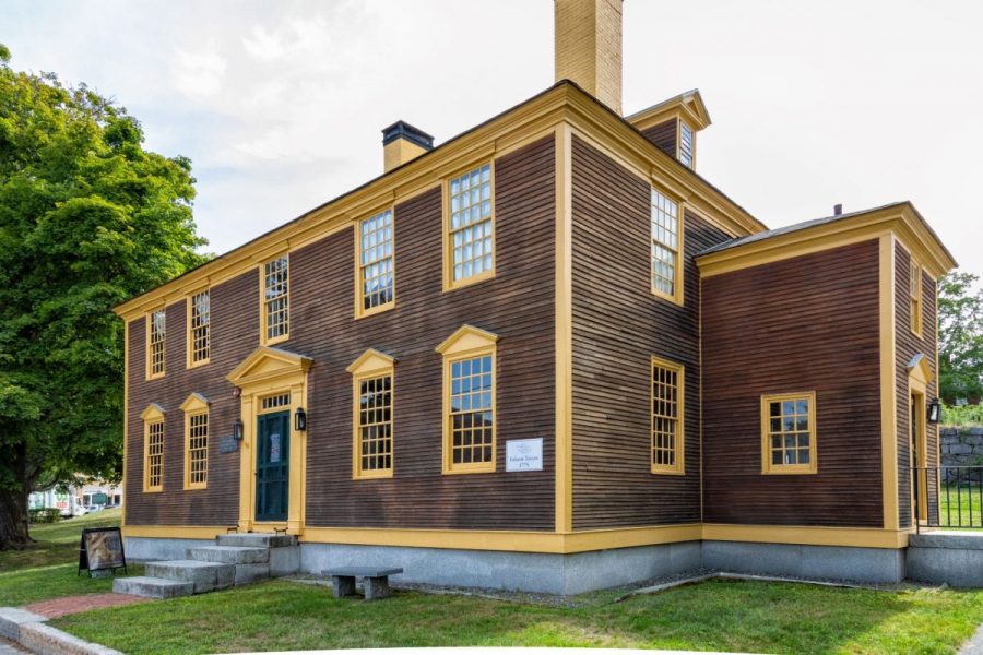 18th century two story wooden tavern with yellow architectural detailing and a dark green door.