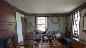 Room in a colonial tavern with three men (some in military uniform) sitting, a woman standing and pouring a drink, and a fourth man walking away.